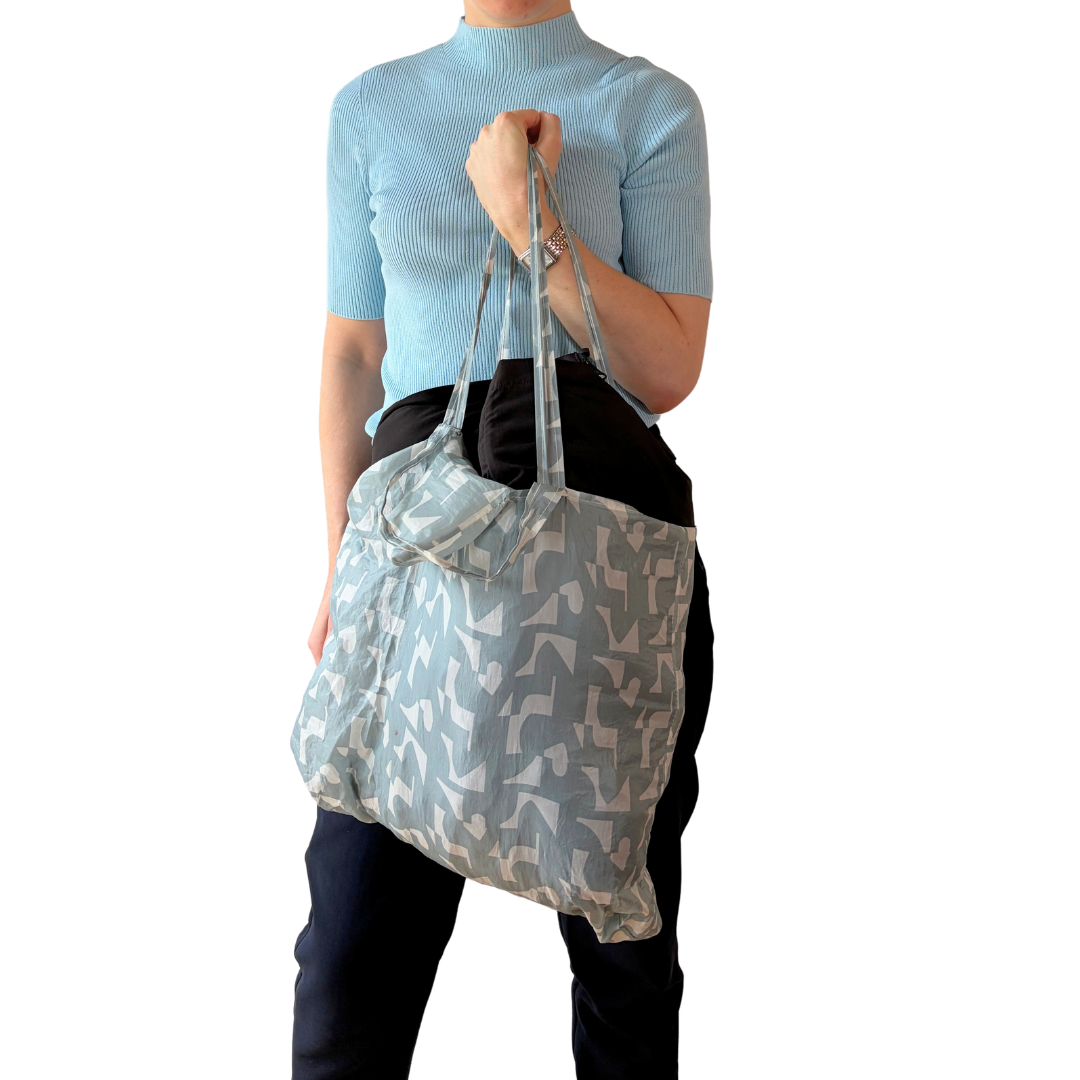 Model in a light blue top carrying a patterned tote bag, CABIN FLEX travel look